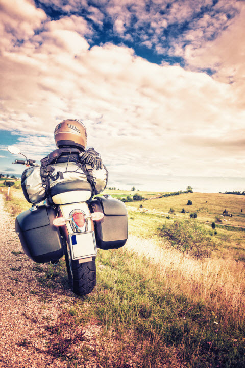 Motorcyclist riding down a country road with blue skies and open spaces in front of him