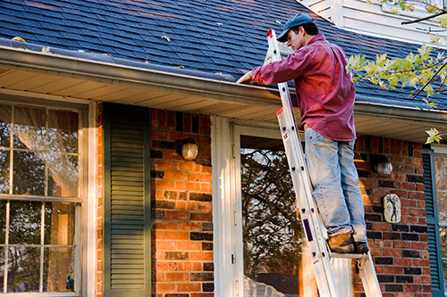 A mobile home owner on ladder cleaning out gutters